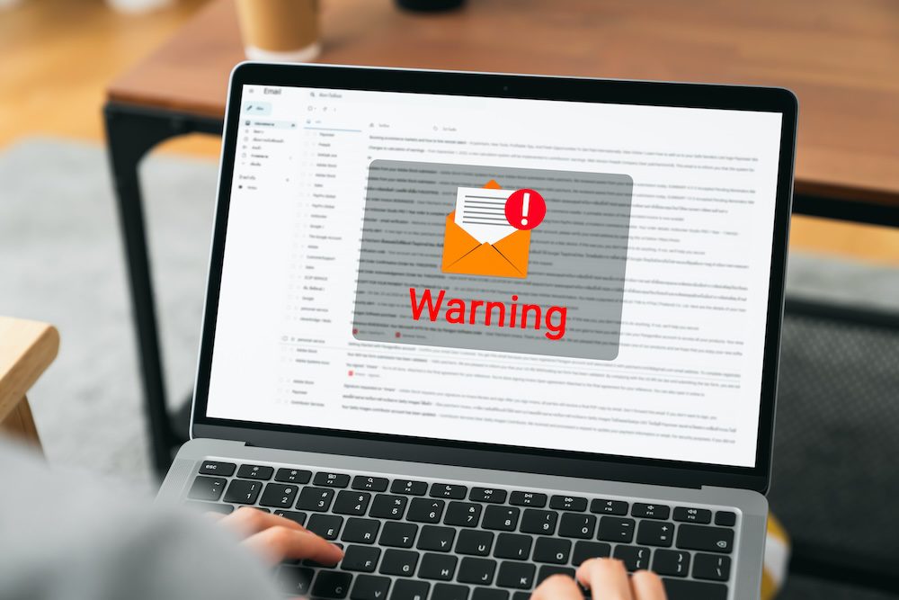 A person using a laptop sees a large warning message with an envelope and exclamation mark icon on the screen, indicating a potential email threat or phishing alert in their inbox, prompting immediate cybersecurity protection.
